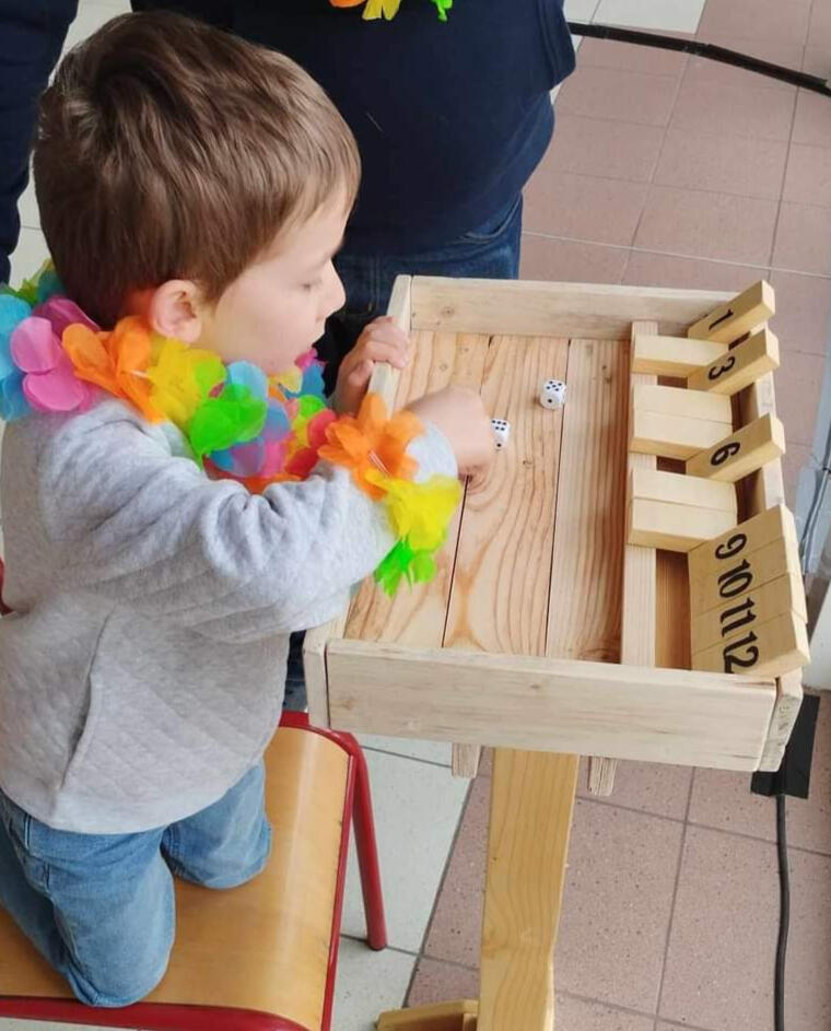 Shut the box Piko Event | Photo du jeu shut the box, un enfant y joue guidé par un adulte. Jeu en bois loué pour anniversaire